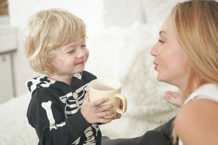 Beautiful little boy enjoying a cup of drink at white home backgroundの写真素材