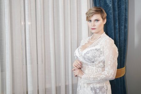 sexy blonde plus size short hair woman in lingerie transparent dress on bedroom backgroundの写真素材