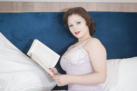 cute retro woman with book enjoy by reading and education on the bed. pretty girl in nightgown in the bedroom.の写真素材