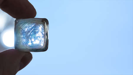 The fingers of the hands hold a square, glass, transparent crystal, there is a free space. The lamp is shining brightly.の写真素材