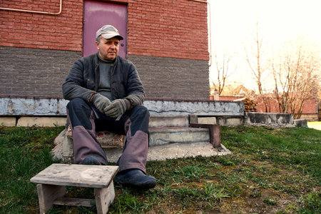 An adult male, of retirement age, sits on the step and looks away. Farmer.の写真素材