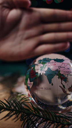 Glass ball globe. Spruce branches are on the table. In the background is a hand gesture.の写真素材