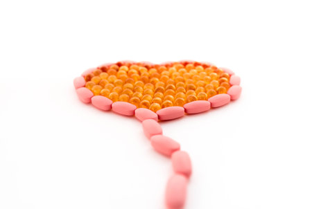 Vitamins of different types, laid out in the form of a heart, on a white isolated background. Pink and dark yellow.の写真素材