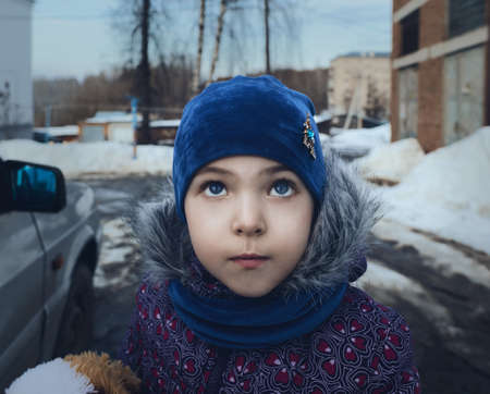 The baby girl looks to the top, winter weather, the onset of spring, selective focus. The concept of children and parents. Blurred background.の写真素材