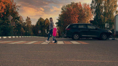 Mother and daughter cross the road at a pedestrian crossing. White-yellow zebra. Pedestrian crossing, marking on the road to cross to the other side.の写真素材