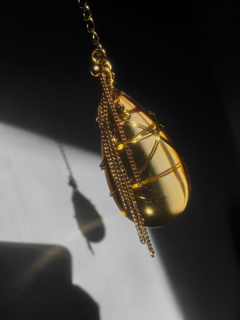 A golden pendant on a chain. Precious yellow stone on the pendant. The gold decoration hangs in the air and casts a shadow. Selective focus.の写真素材