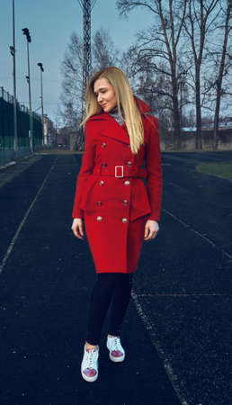 The girl in the red coat stands and looks away. The girl on the opposite court. Stylish red coat. Autumn clothingの写真素材