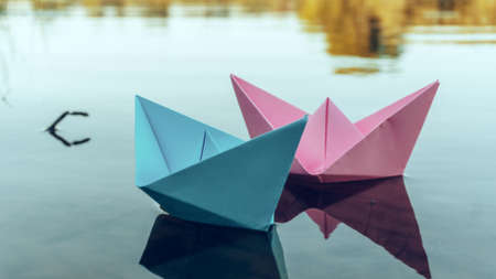Two paper boats of red and blue color, floating on the water. Summer day on the river bank. Playing with paper boats.の写真素材