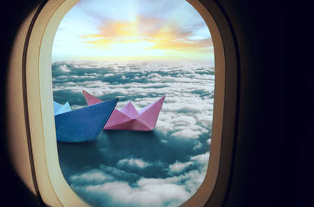The window of the plane through which you can see how two ships of pink and blue float in the clouds, the sun shines against the background.の写真素材