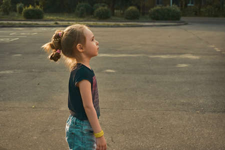 The baby girl stands on the pavement and looks away. The sun illuminates the hair and contour.の写真素材