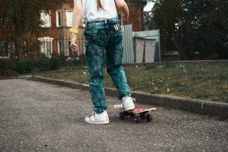 A baby girl stands in a aswalt parking lot and learns to skateboard. Girl in jeans, white T-shirt...