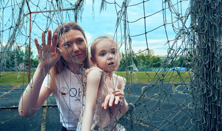 Mom and daughter hold on to the torn net from the goalkeeper's gate. Summer day for sports and...