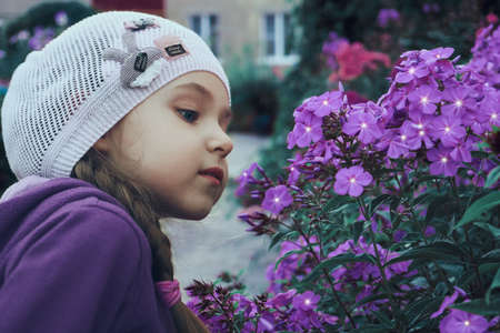 A girl in a pink hat and purple jacket, looks at beautiful purple flowers. The flowering period of ornamental plants.の写真素材