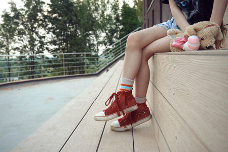 A girl child with soft toys sits on a bench in the park, a place to relax and walk. Sunny summer...