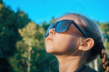 A girl child in sunglasses looks at the top in the direction of the sun. Selective soft selective...