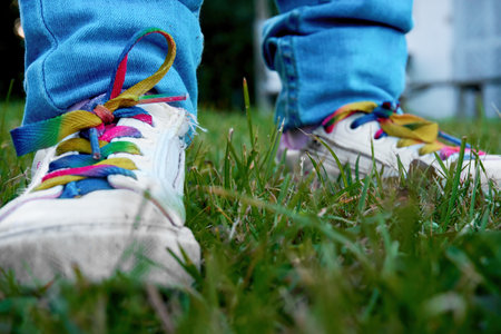 A child in blue jeans and white beauties with colorful laces, standing on the green grass. Selective selective soft focus.の写真素材