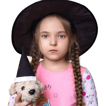 A girl child with pigtails looks directly into the camera, on the head of a large black, round hat in the hands of a plush toy dog with a cap on its head. selective focus.の写真素材