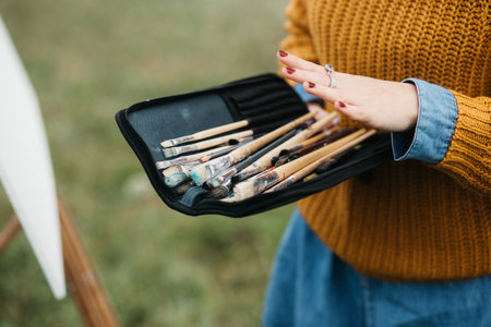 Close up photo of young female artist working on painting outdoors. She holds oil paints, artist...