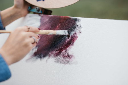 Close up photo of young female artist working on painting outdoors. She holds oil paints, artist...