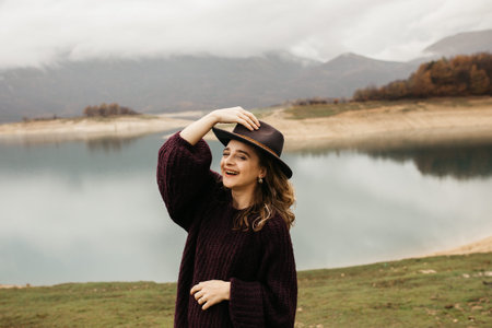 Happy beautiful woman in purple sweater holding her hat and enjoying trip on the lake. Female...