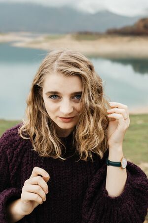 Outdoors portrait of young woman with curly hair wearing fashionable wrist watch. She is standing near lake.の写真素材