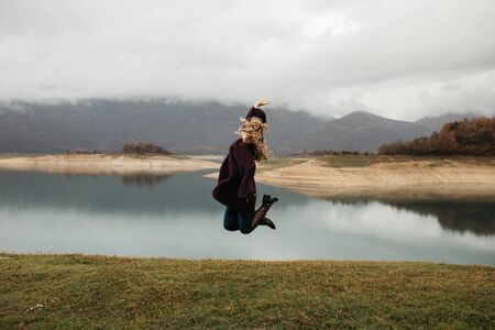 Happy young woman in purple sweater and boots jumping on the lake.の写真素材