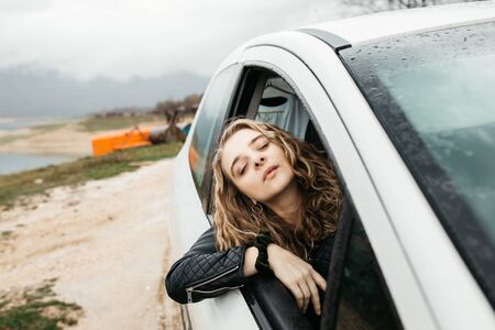 Beautiful young woman looking through open window of the car while it iss raining outside.の写真素材