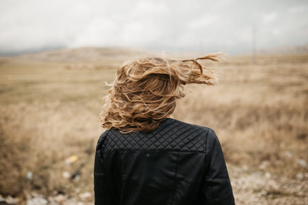 Portrait of young woman with hair blowing in the wind. She is  wearing a leather jacket with a...