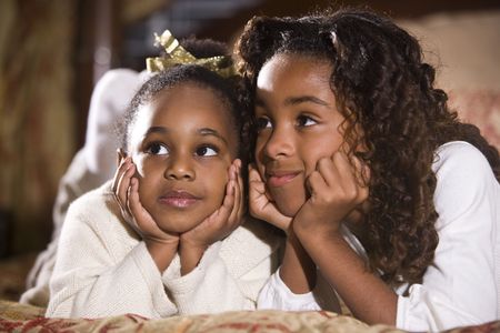 Happy four and ten year old African American sisters sitting together in bedroomの写真素材