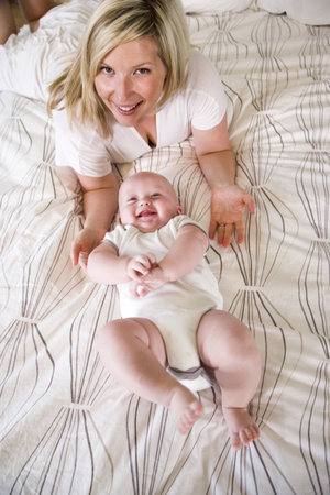 Mother lying on bed with cheerful seven month old baby