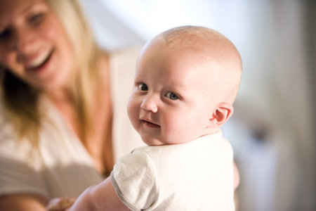 Closeup of seven month old baby looking over his shoulder, with mother in background
