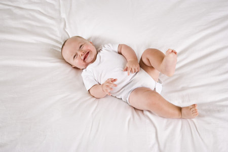 Cute six month old baby laughing while lying on white bed