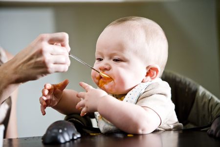 Six month old baby eating solid food from a spoonの写真素材