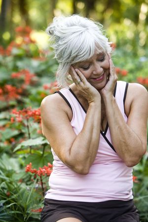 Woman in her 50s standing in park surrounded by greenery, looking contentの写真素材