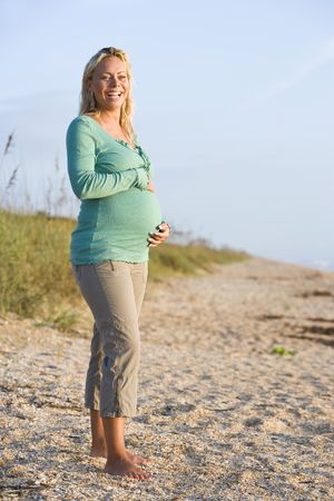 Happy young pregnant woman in her 20s standing on sand at beachの写真素材