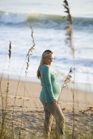 Side view of smiling pregnant woman standing on beachの写真素材