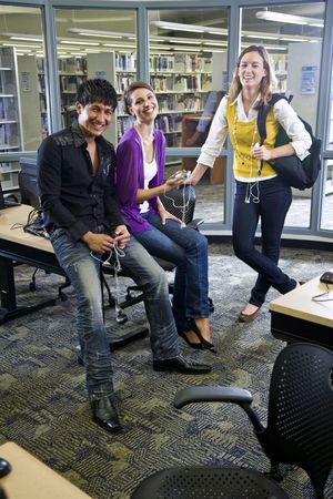 Three university students looking at music players in school libraryの写真素材
