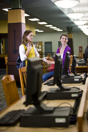 Two young female college students standing next to computers in school library