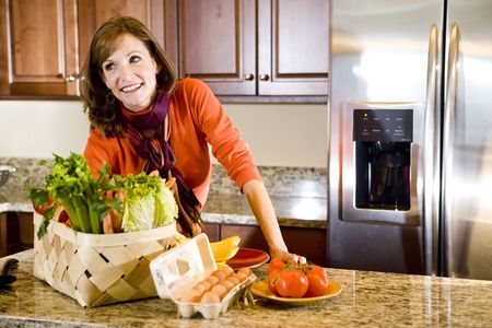 Happy attractive mature woman in kitchen with fresh produce on counterの写真素材