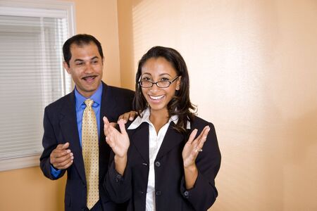 Young happy African-American female office worker standing in boardroom with middle-aged Hispanic manager smiling behind with hand on her shoulderの写真素材