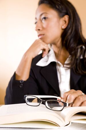 Serious young African-American woman thinking, focus on eyeglasses on bookの写真素材