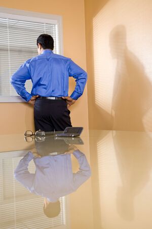 Middle-aged Hispanic businessman in boardroom looking out office windowの写真素材