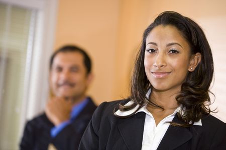 Confident young African-American businesswoman with middle-aged Hispanic male co-worker in backgroundの写真素材