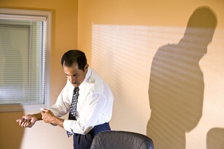 Middle-aged Hispanic businessman rolling up sleeve looking down reading in boardroomの写真素材