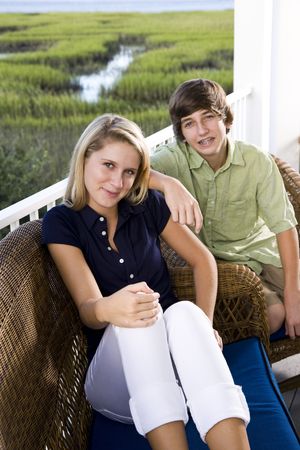 Teenage girl and younger brother sitting together on terrace smilingの写真素材