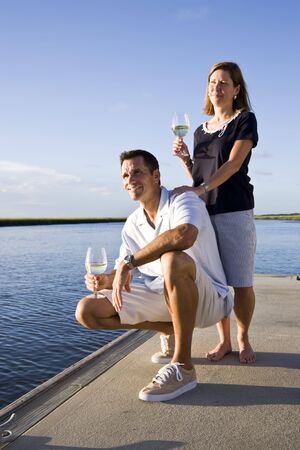 Mid-adult couple on dock by water enjoying drink on sunny dayの写真素材