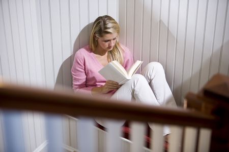 17 year old teenage girl reading alone in quiet corner by staircaseの写真素材