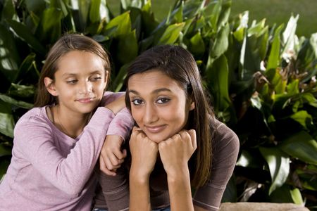 Pretty mixed-race Indian teen girl smiling with 10 year old sister leaning on shoulderの写真素材