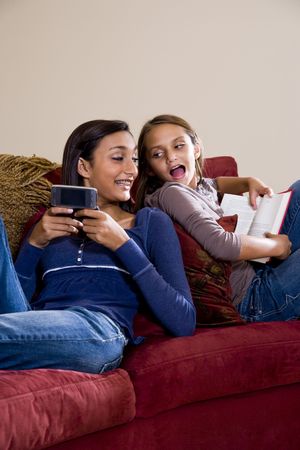 Teen girl texting on mobile phone while younger sister reads bookの写真素材