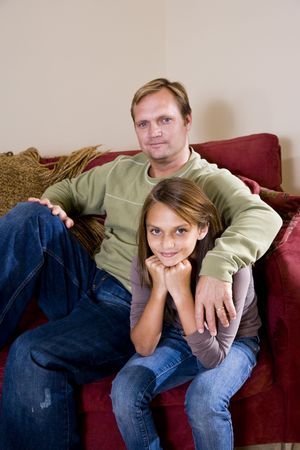 Portrait of young girl with father sitting at home on sofaの写真素材
